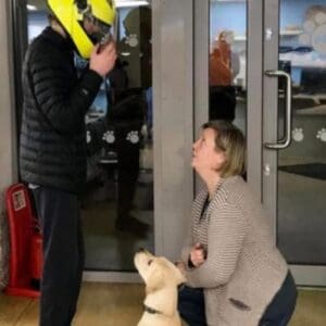 A lady and her dog looking up at a person in a yellow motorbike helmet